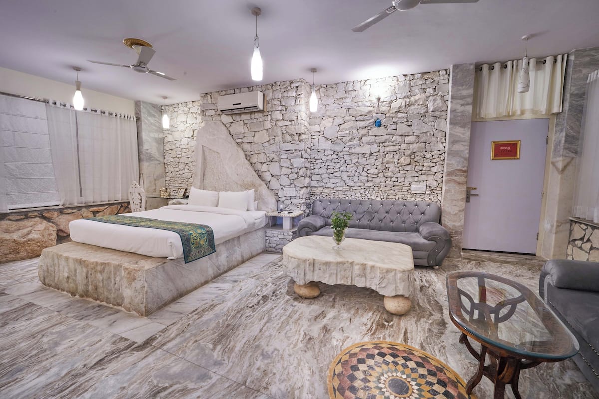 A modern room with a stone wall, a sofa, a coffee table, and a bed with a white bedspread.