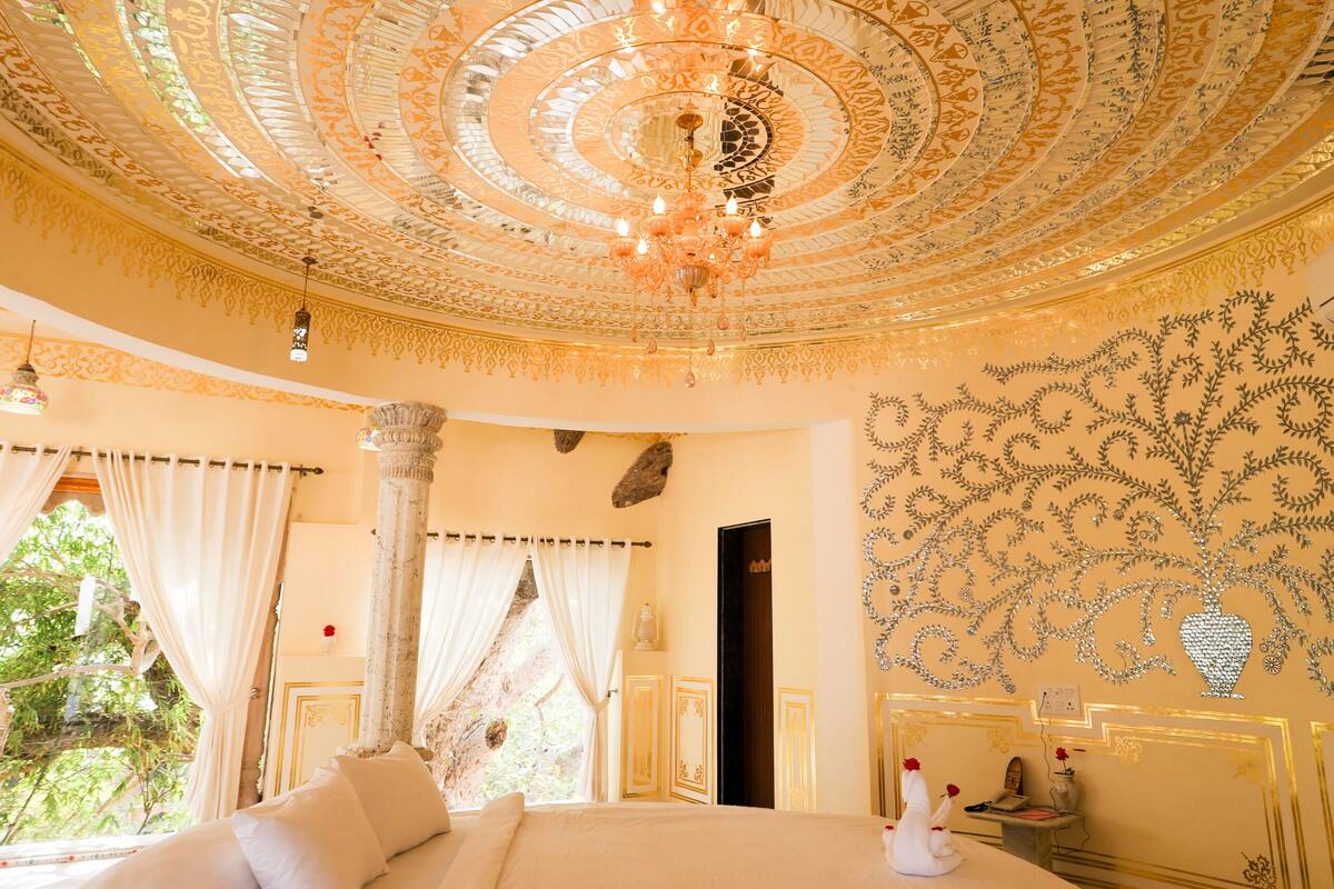 A circular bed with a white bedspread, a chandelier, and ornate ceiling patterns.