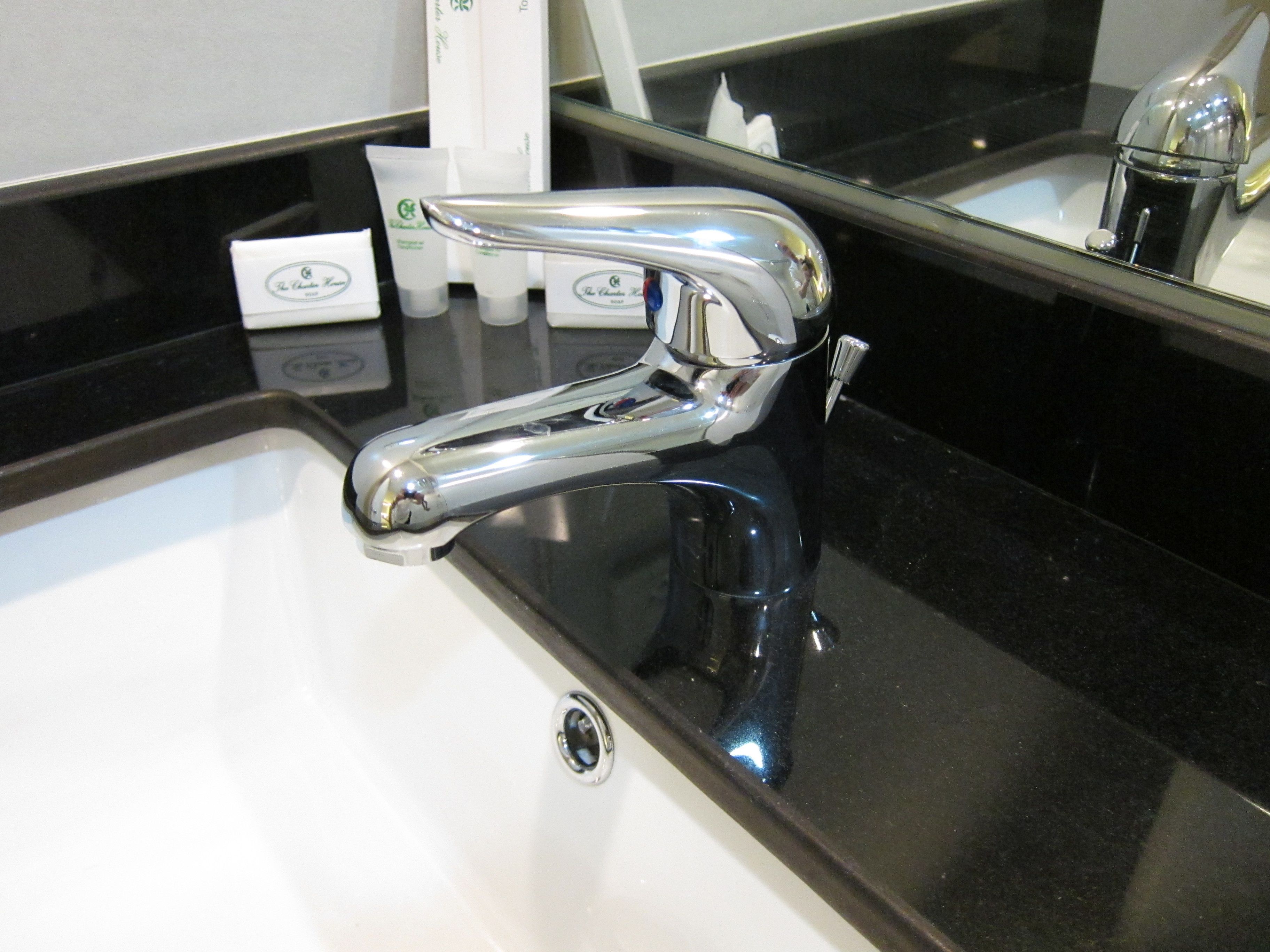 A modern bathroom with a chrome faucet, a black countertop, and a mirror reflecting the sink area.