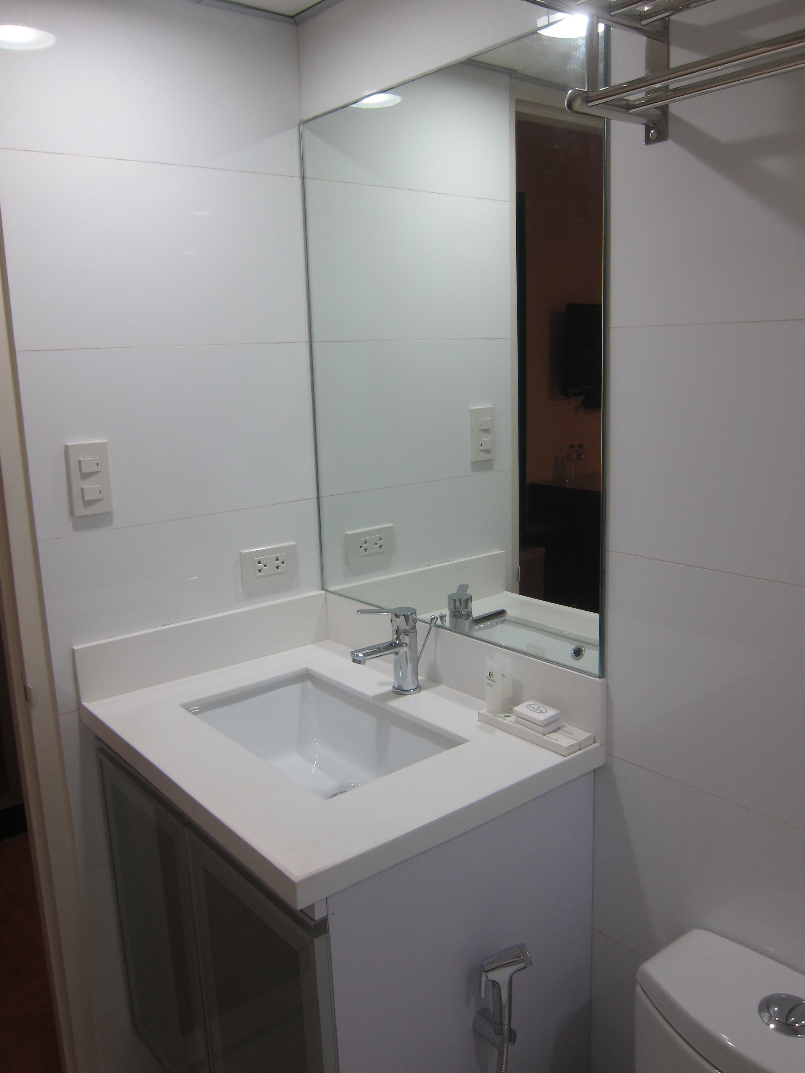 Un baño con lavamanos, espejo e inodoro blancos.