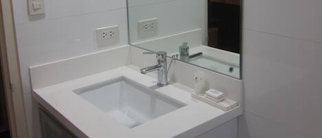 Un baño con lavamanos, espejo e inodoro blancos.