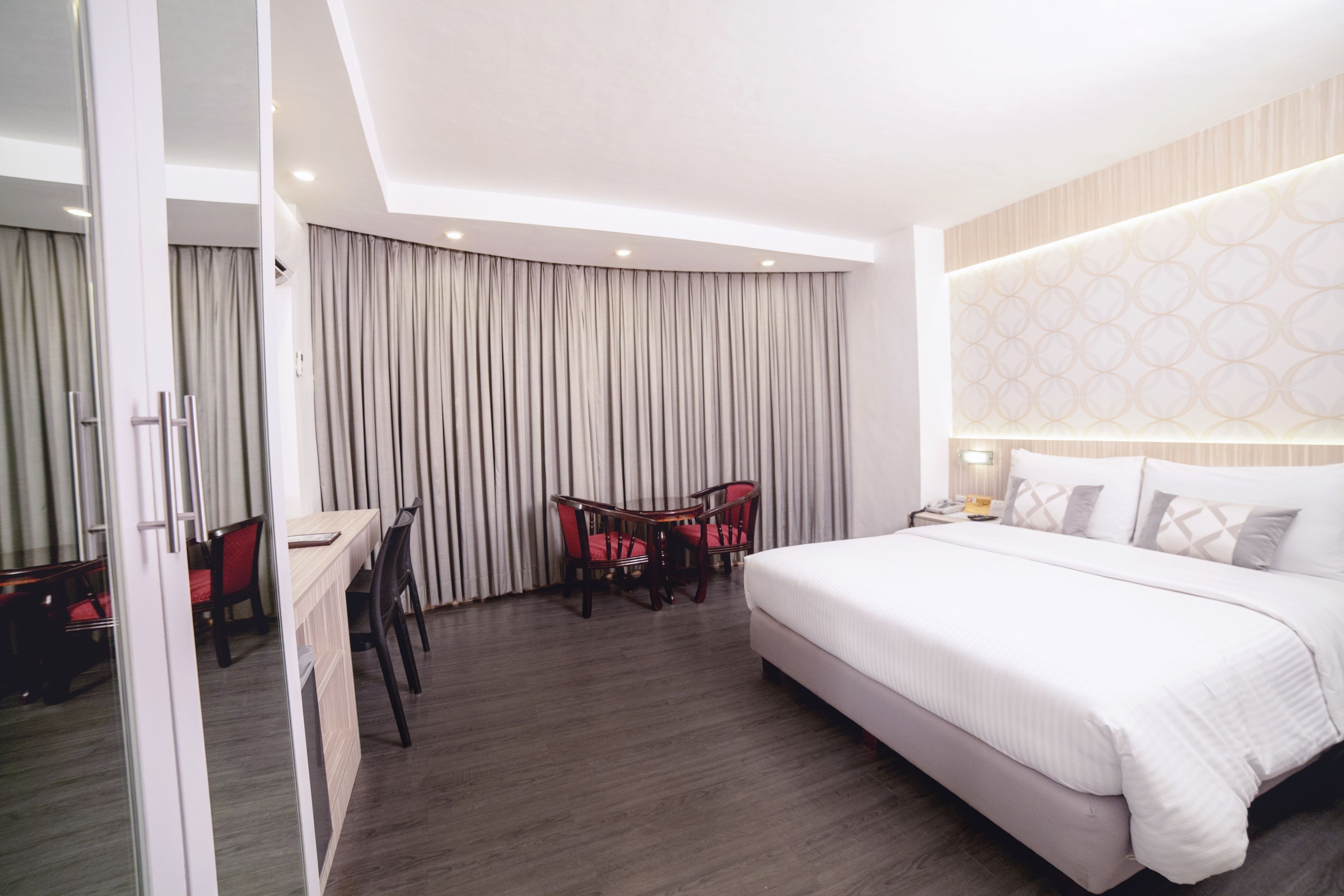Une chambre d’hôtel avec un grand lit, un bureau avec deux chaises et un rideau qui sépare l’espace nuit de l’espace de travail.