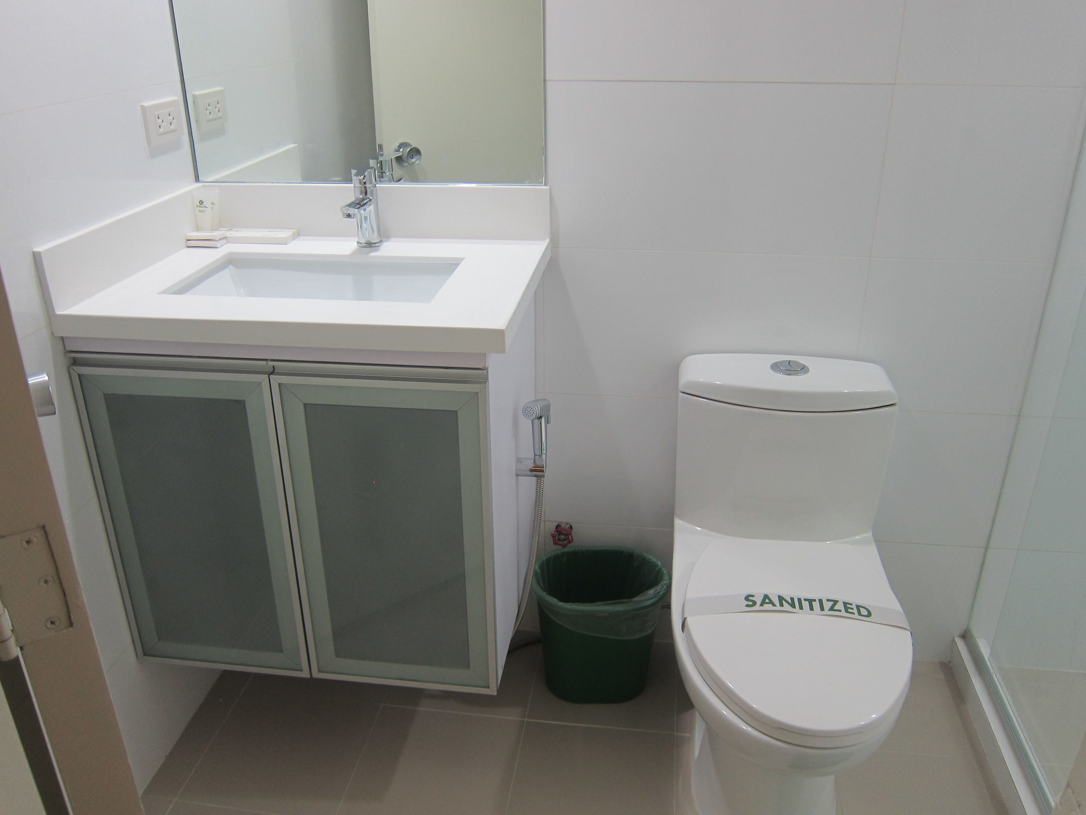 A bathroom with a white sink, a toilet, and a green trash bin.