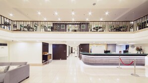 A spacious lobby with a reception desk, a grey sofa, and a balcony with decorative railings. - The Charter House (Makati)