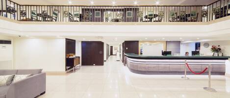 A spacious lobby with a reception desk, a grey sofa, and a balcony with decorative railings.