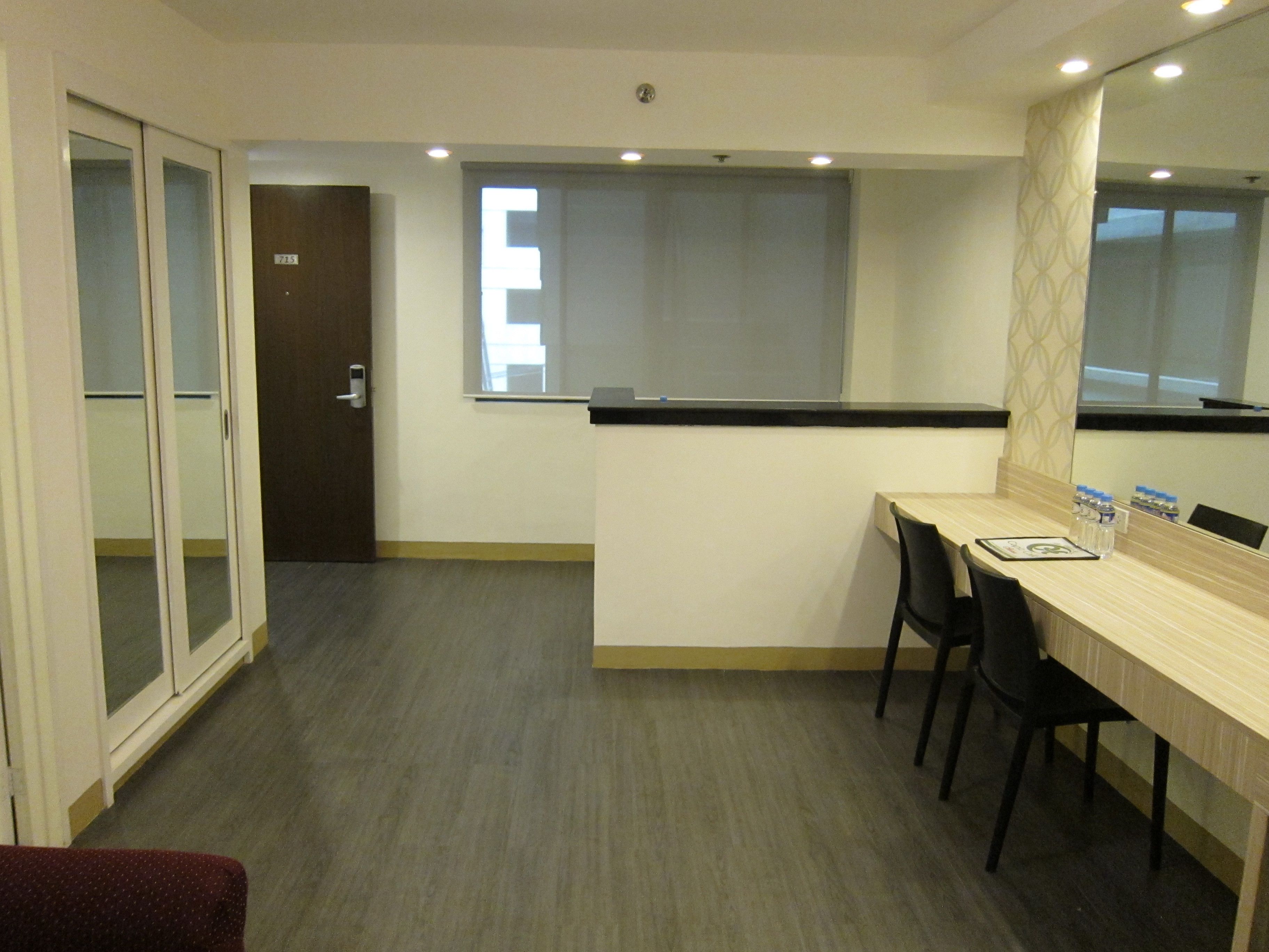 A hotel room with a wooden desk, two chairs, a small window, and a door.