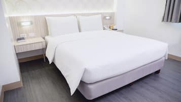A neatly made bed with white linens, a bedside table with a lamp, and a wall-mounted light fixture.