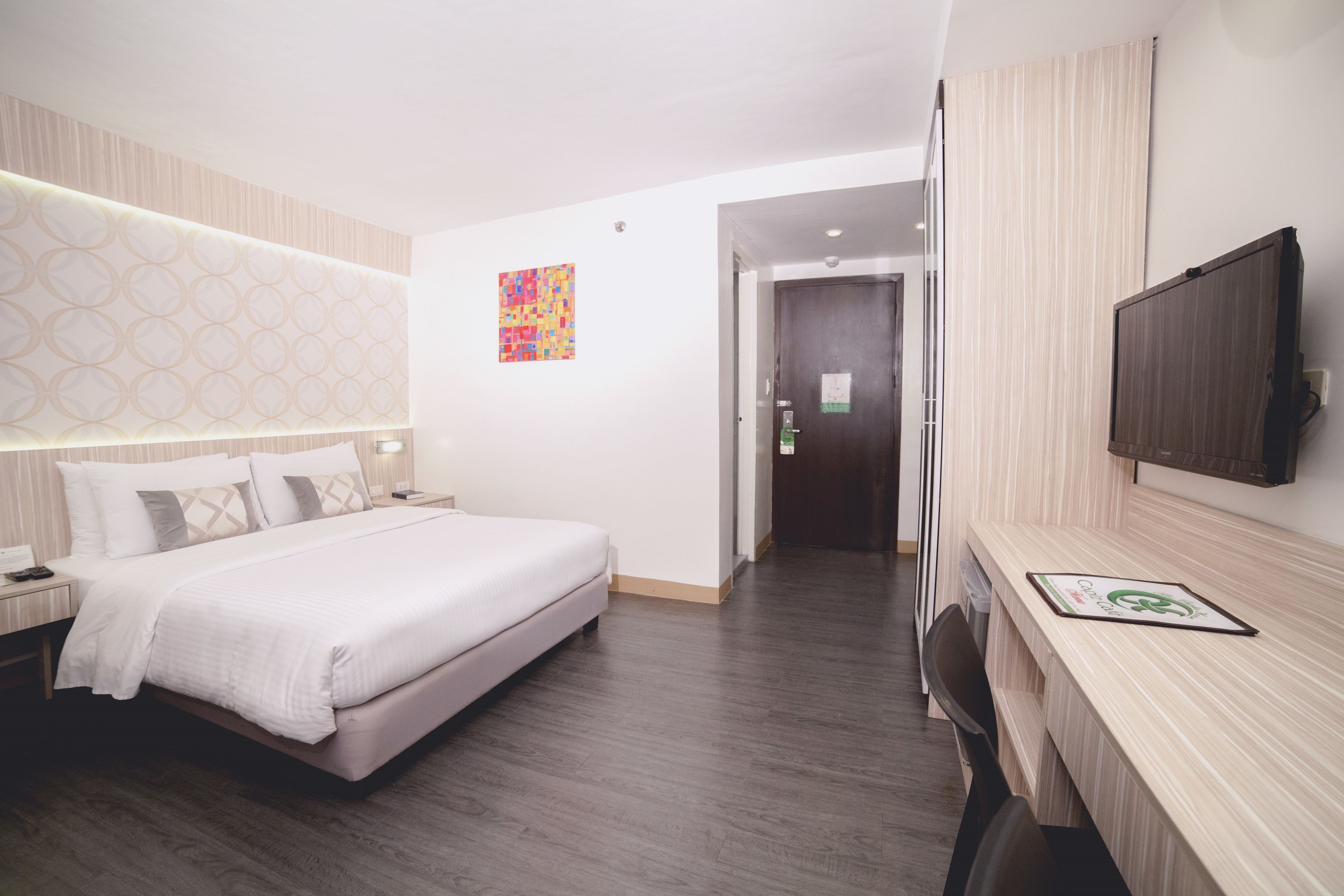 A hotel room with a bed, bedside table, lamp, and a TV mounted on the wall.