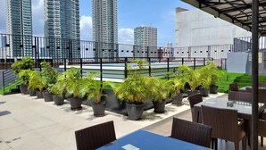A rooftop terrace with potted plants, outdoor seating, and a view of tall buildings. - The Charter House (Makati)