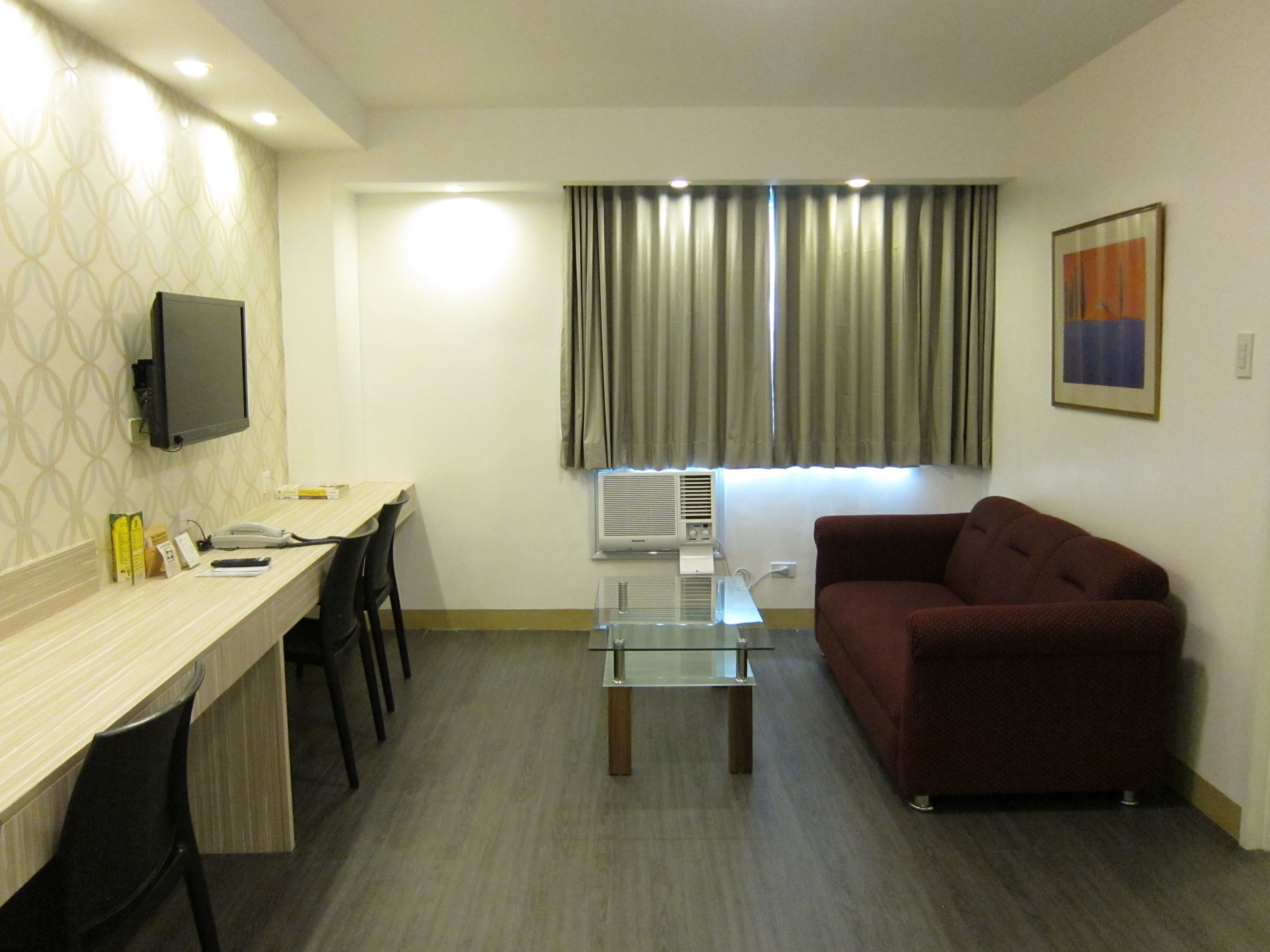 A compact living space with a desk, chairs, a sofa, a TV, and a window with curtains.