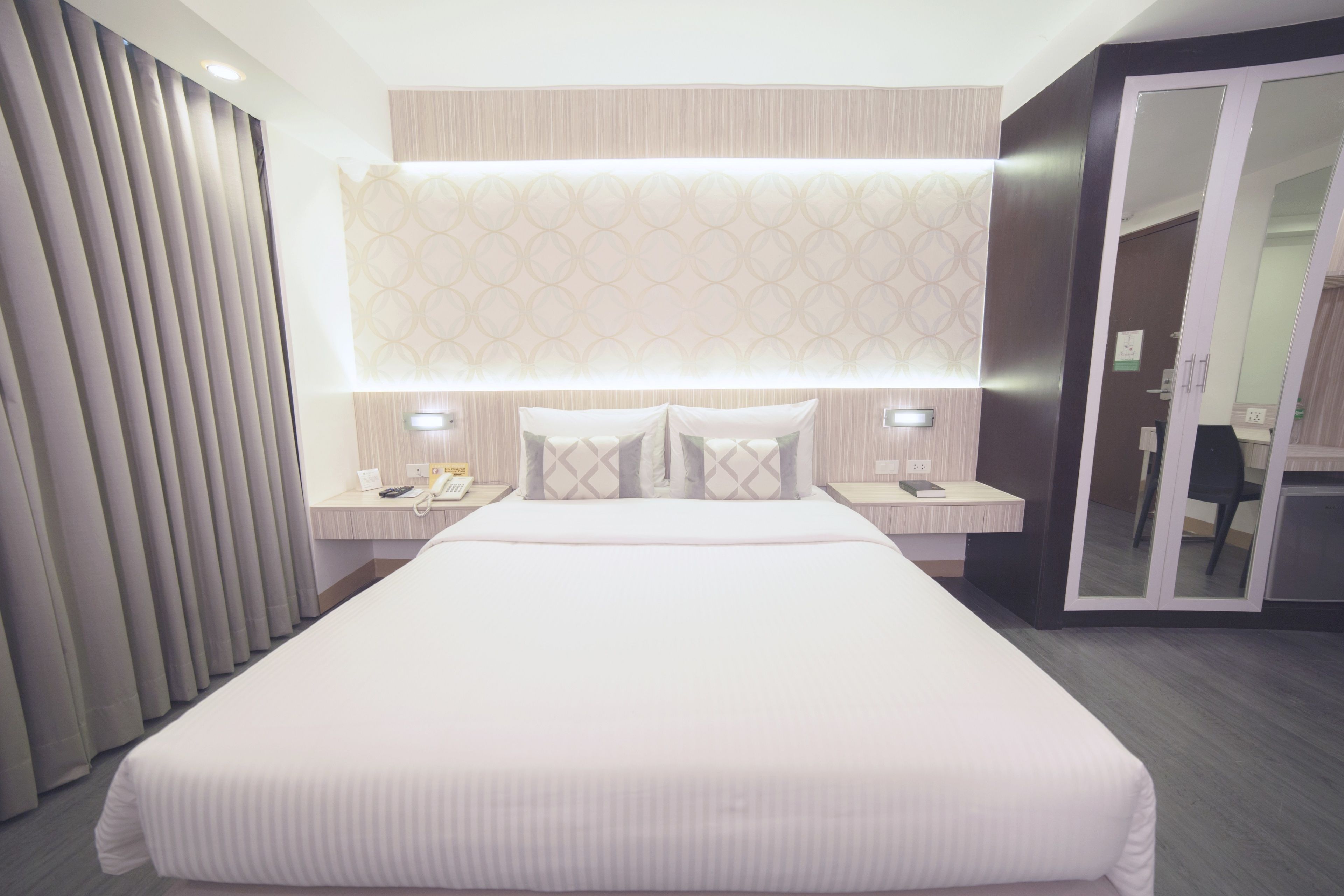 A modern hotel room with a large bed, bedside tables, and a mirror.