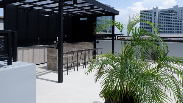 A rooftop bar with a modern design, featuring a black pergola, a bar counter, and several seating areas. - The Charter House (Makati)