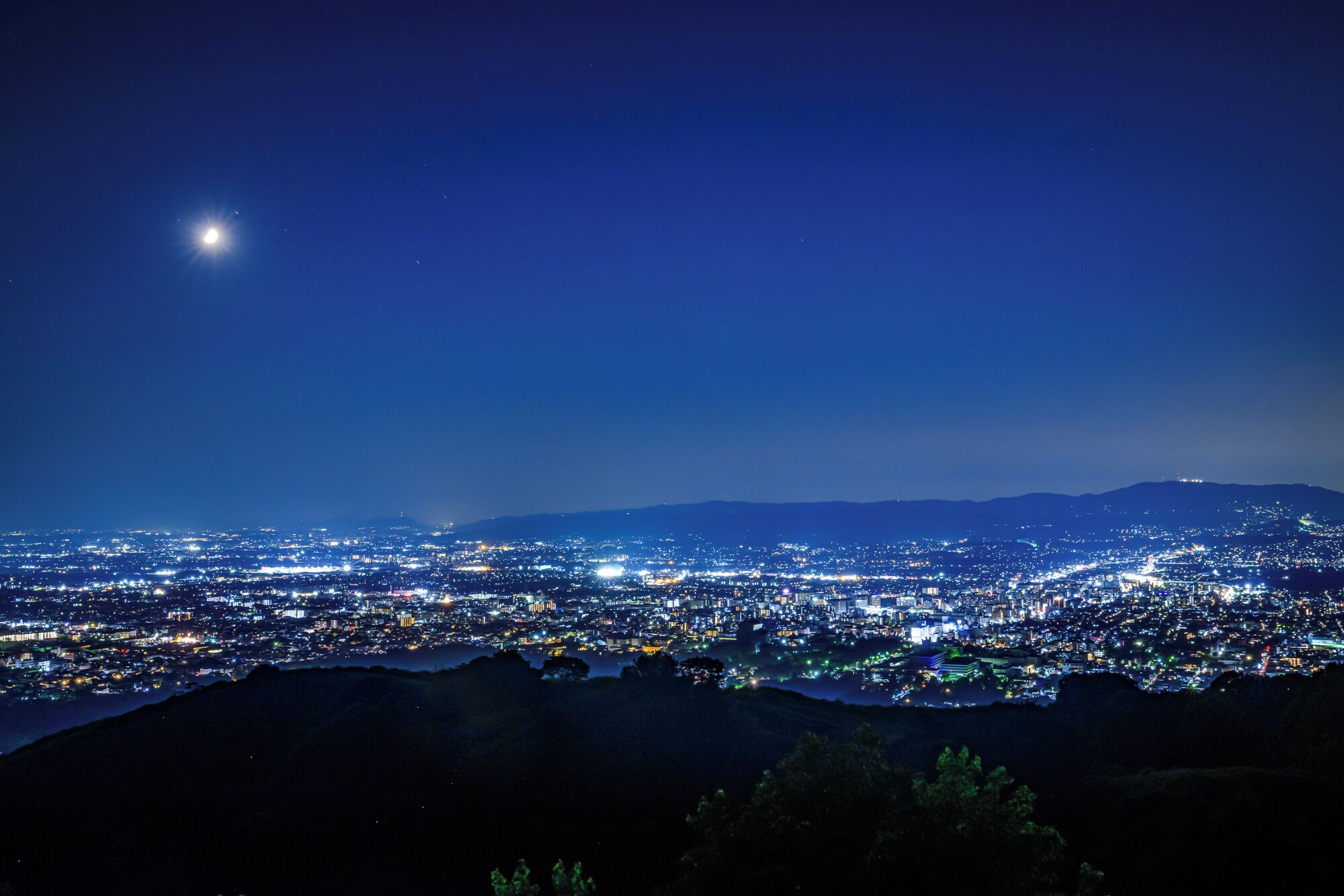 Un paisaje urbano nocturno con cielo estrellado y una luna destacada.