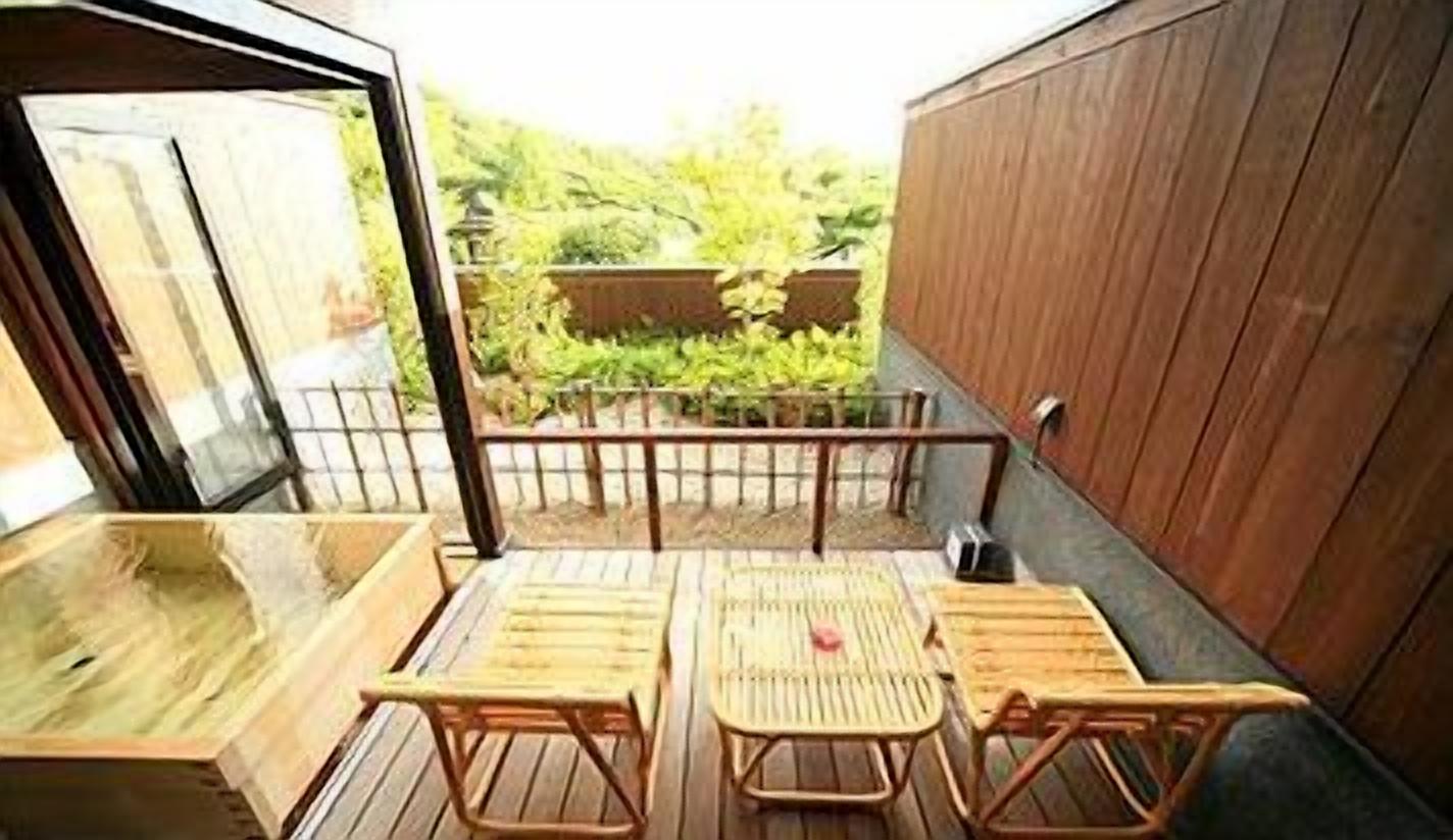 A wooden deck with a table and chairs, a wooden wall, and a view of greenery.