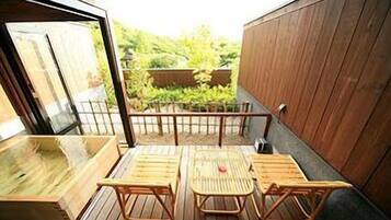 A wooden deck with a table and chairs, a wooden wall, and a view of greenery.