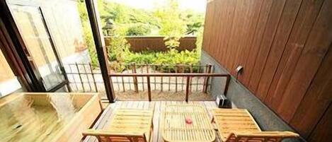 A wooden deck with a table and chairs, a wooden wall, and a view of greenery.