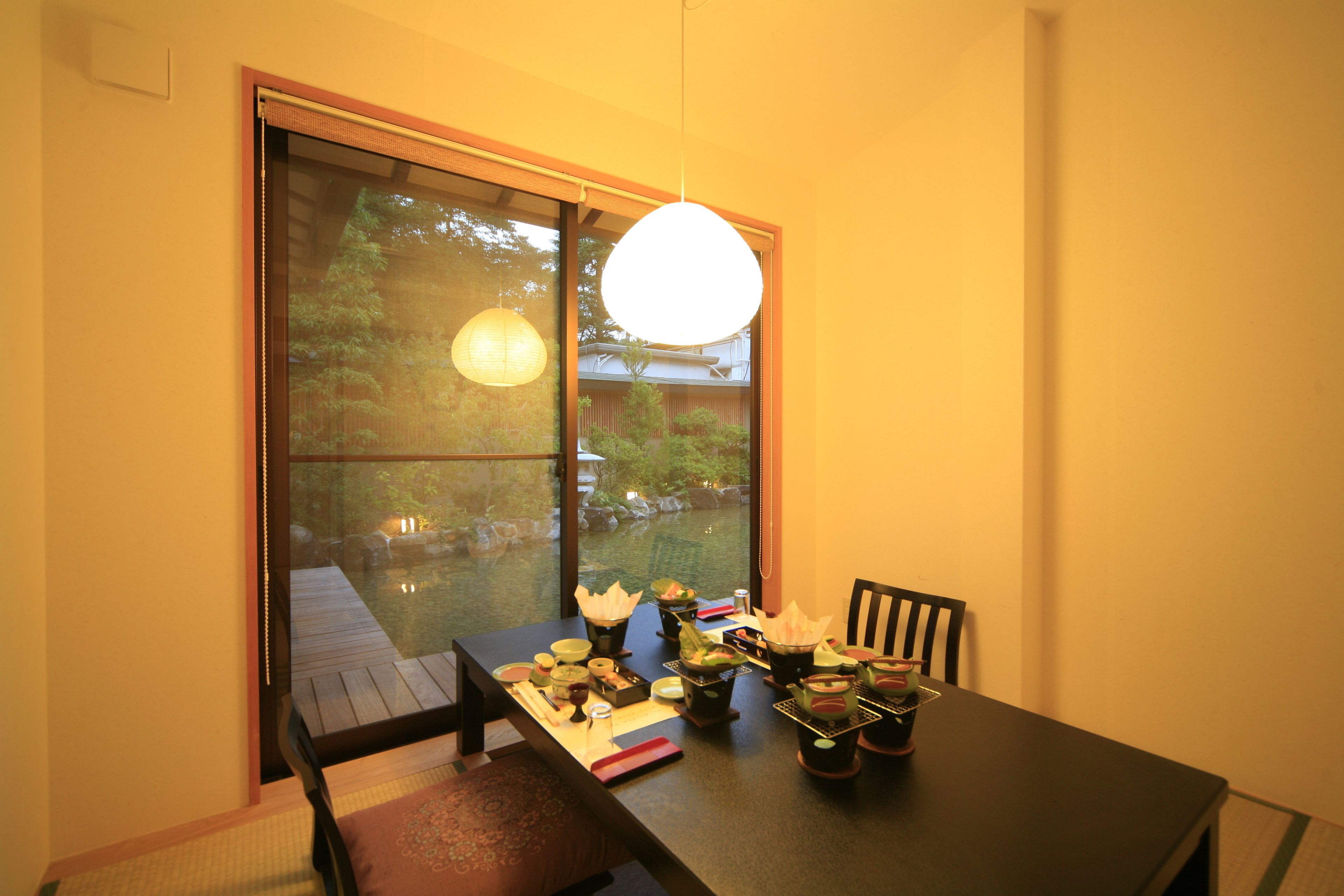 A dining table set with various dishes, a hanging light fixture, and a view of a garden through a sliding door.