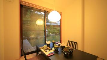 A dining table set with various dishes, a hanging light fixture, and a view of a garden through a sliding door.