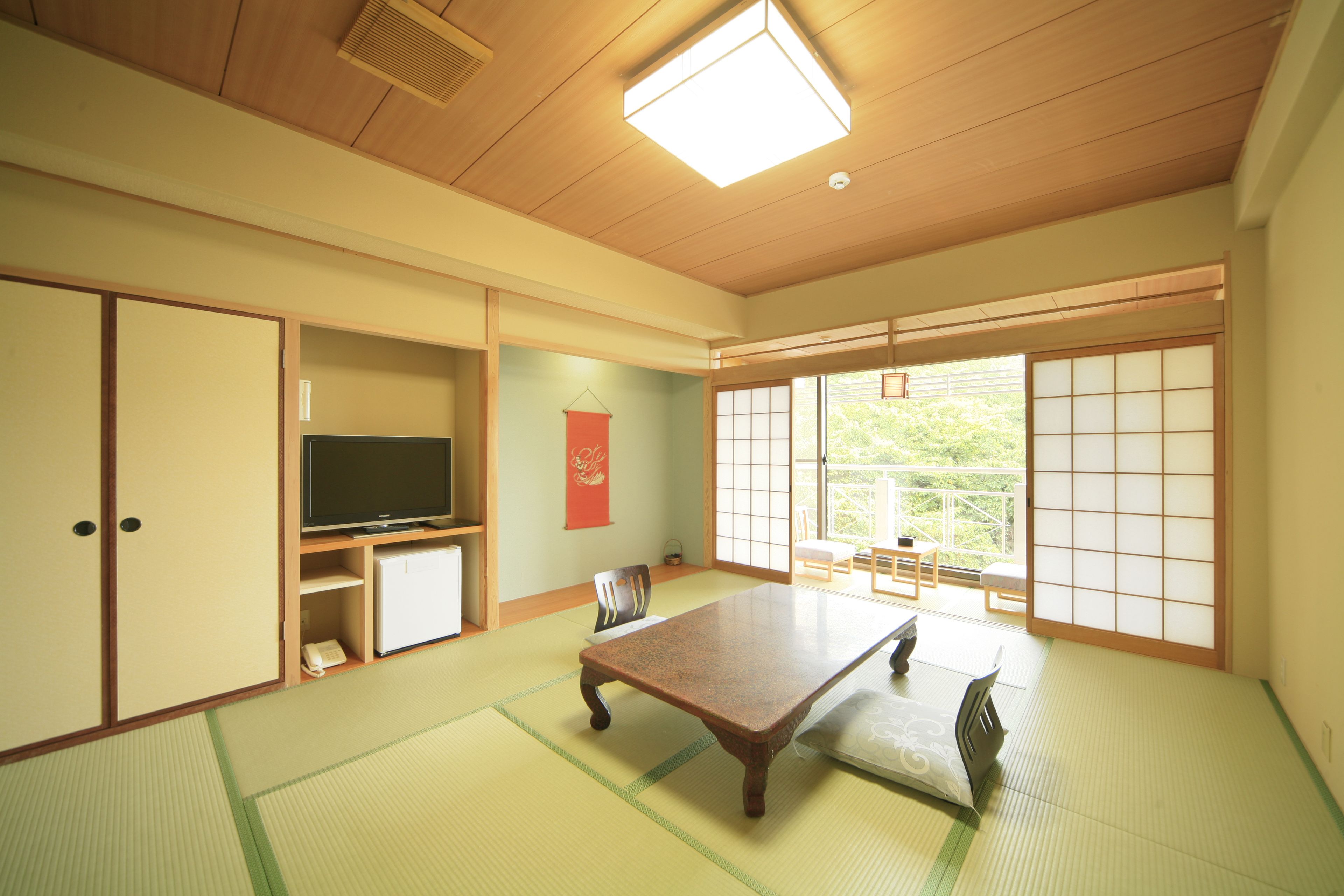 A traditional Japanese room with tatami flooring, a low table, a television, and sliding doors leading to a balcony.