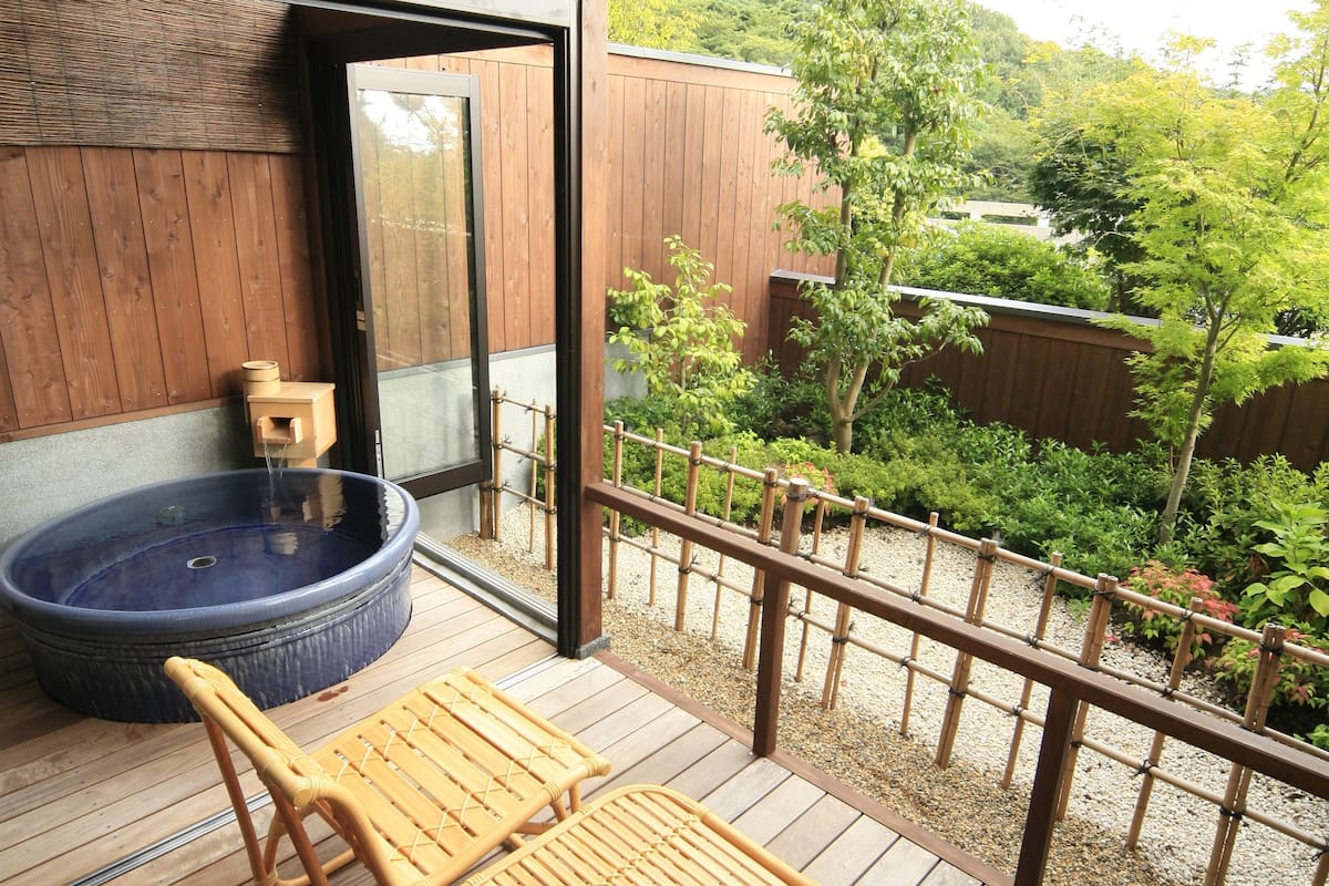 Eine Holzterrasse mit einem Whirlpool, zwei Korbstühlen und einem Tisch.