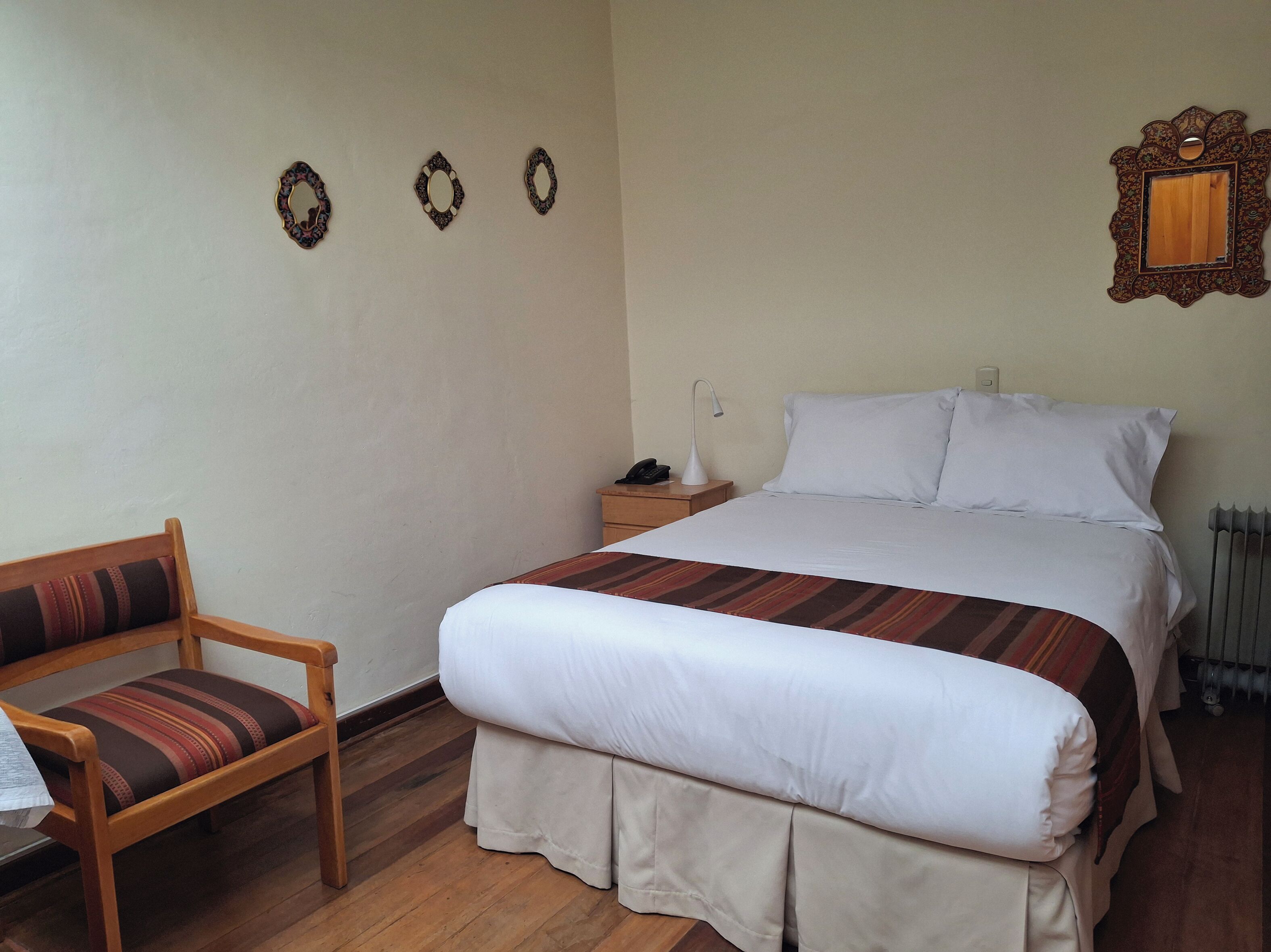 A neatly arranged hotel room with a bed, a chair, a nightstand, and a wall-mounted mirror.