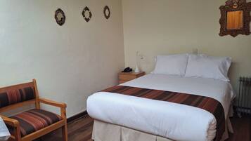 A neatly arranged hotel room with a bed, a chair, a nightstand, and a wall-mounted mirror.