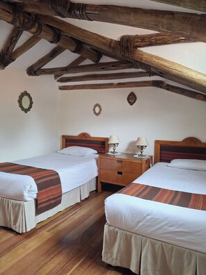 Une chambre avec deux lits, un plancher en bois et des poutres apparentes en bois au plafond.