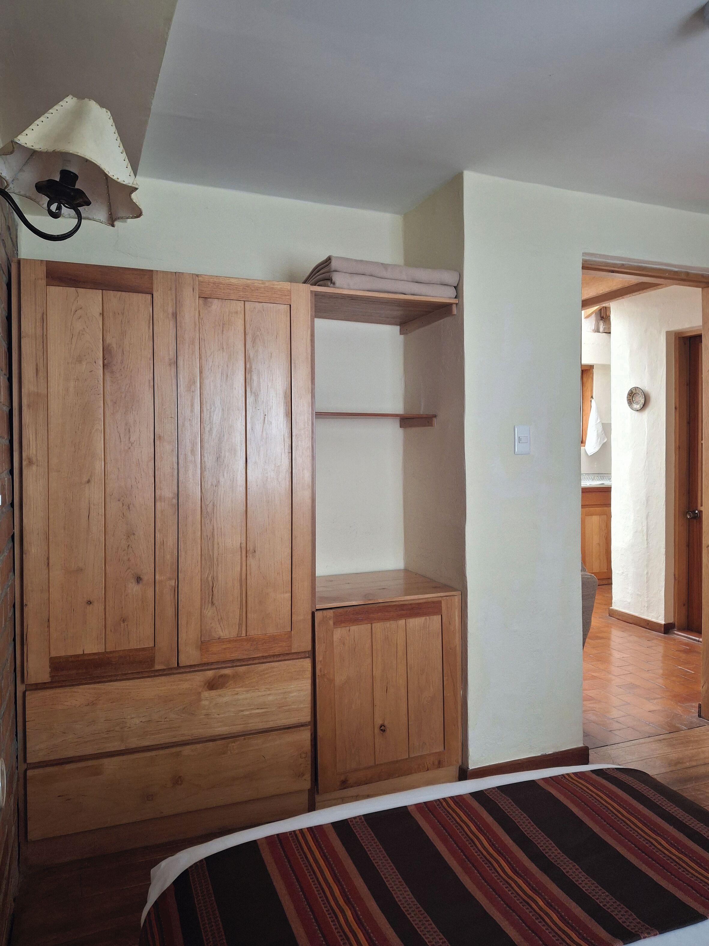 A bedroom with wooden furniture, a bed with a striped bedspread, and a hallway leading to a bathroom.