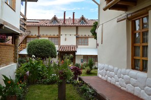 Il s’agit d’un bâtiment traditionnel, doté d’un toit en tuiles, d’un mur en pierre et d’un jardin où poussent diverses plantes et fleurs.