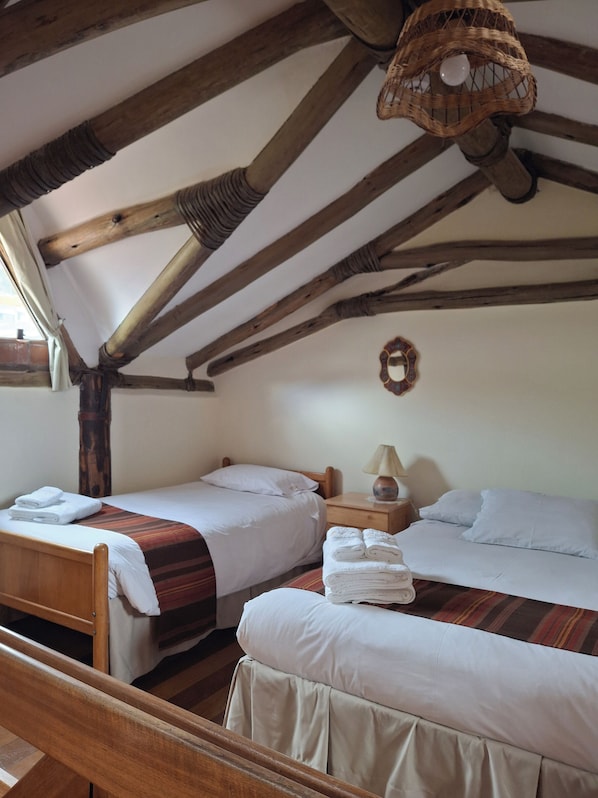 Una habitación acogedora con dos camas, vigas de madera, una lámpara colgante y una mesita con lámpara.