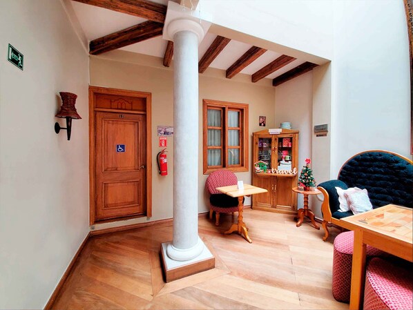 A cozy room with a wooden door, a white column, a small table, a chair, a cabinet with glass doors, and a Christmas tree.