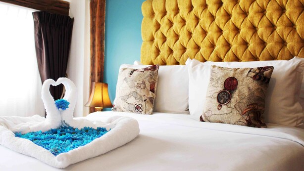 A hotel room with a tufted headboard, a swan-shaped centerpiece, and patterned pillows.