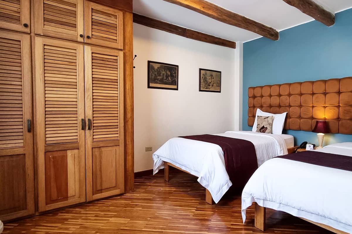 A bedroom with two beds, wooden wardrobe, and a blue accent wall.
