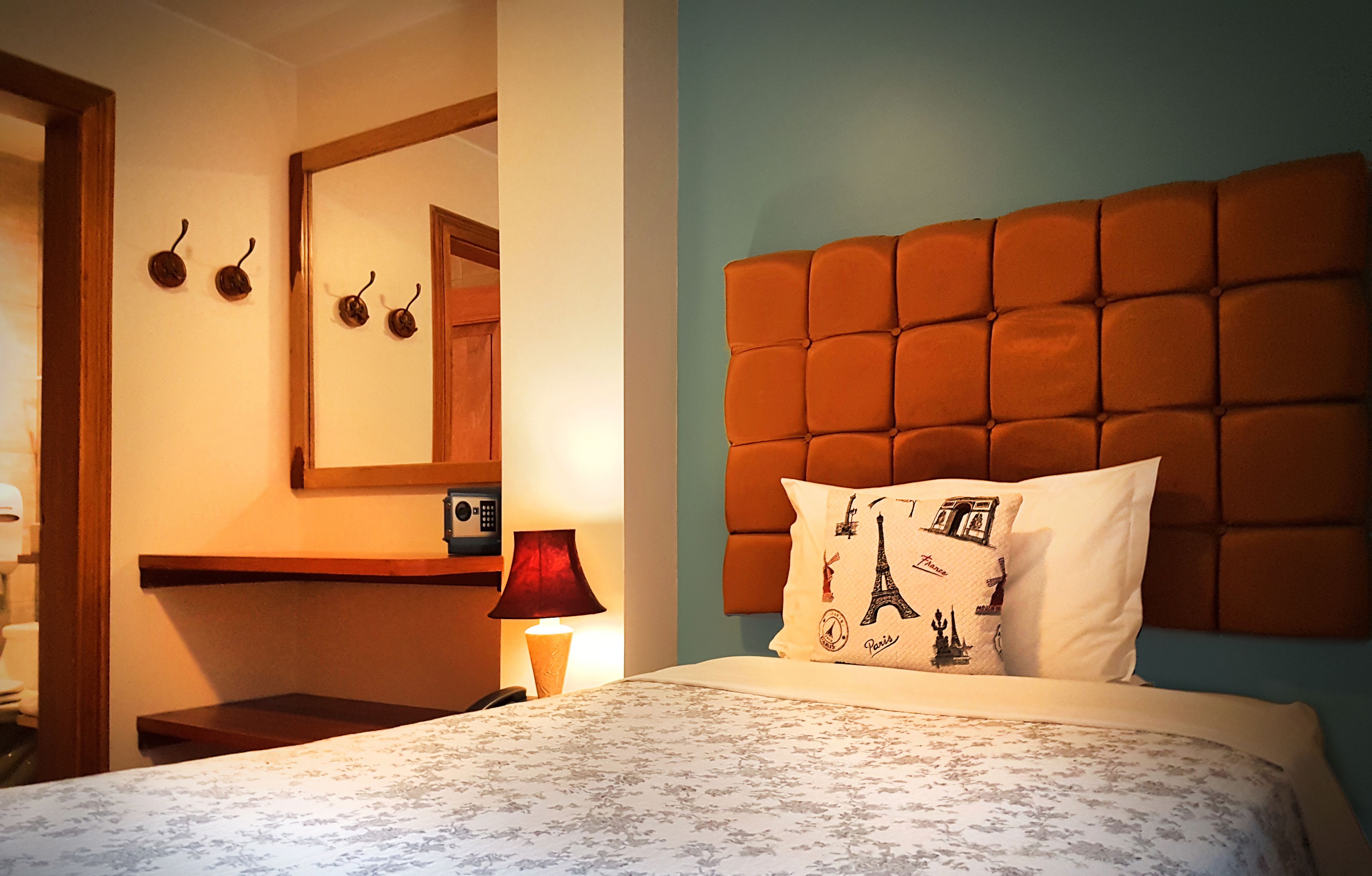 Une chambre d’hôtel comprenant un lit, une table de chevet, une lampe, un miroir et un mur avec une étagère en bois.