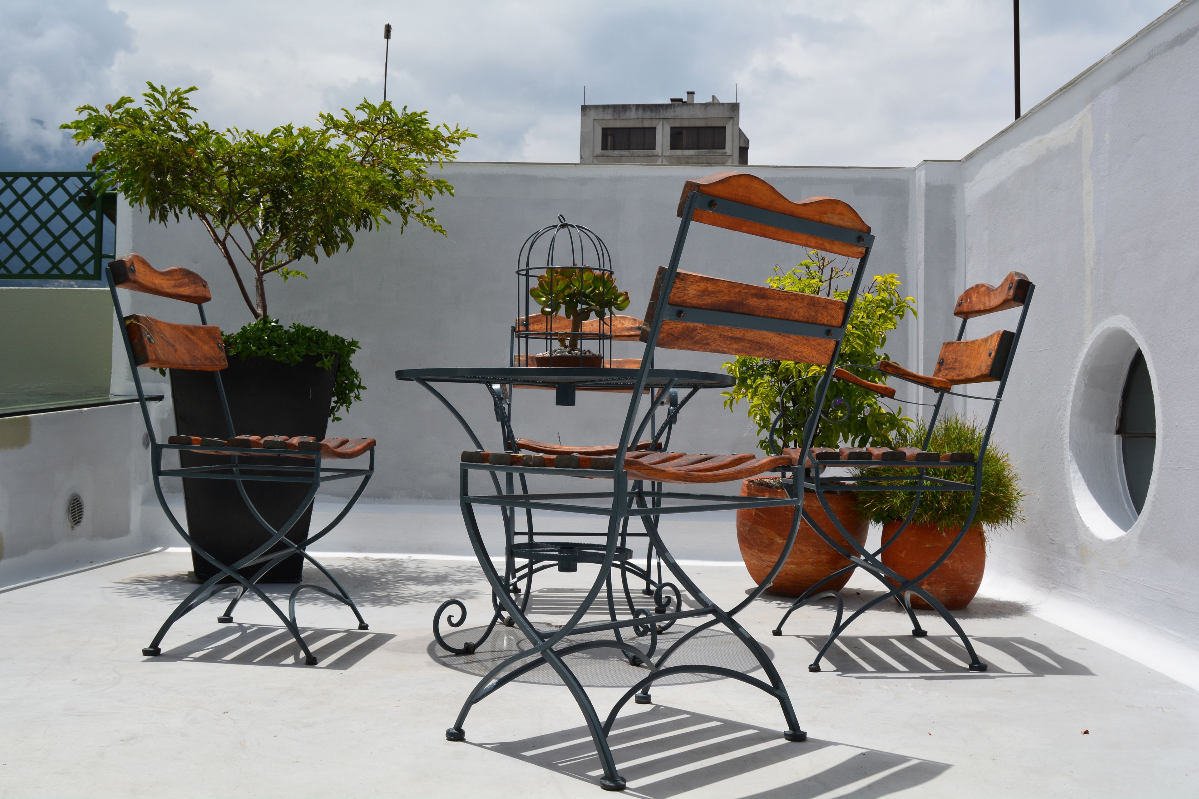 Terraza en la azotea con una mesa y dos sillas, rodeada de plantas en macetas.