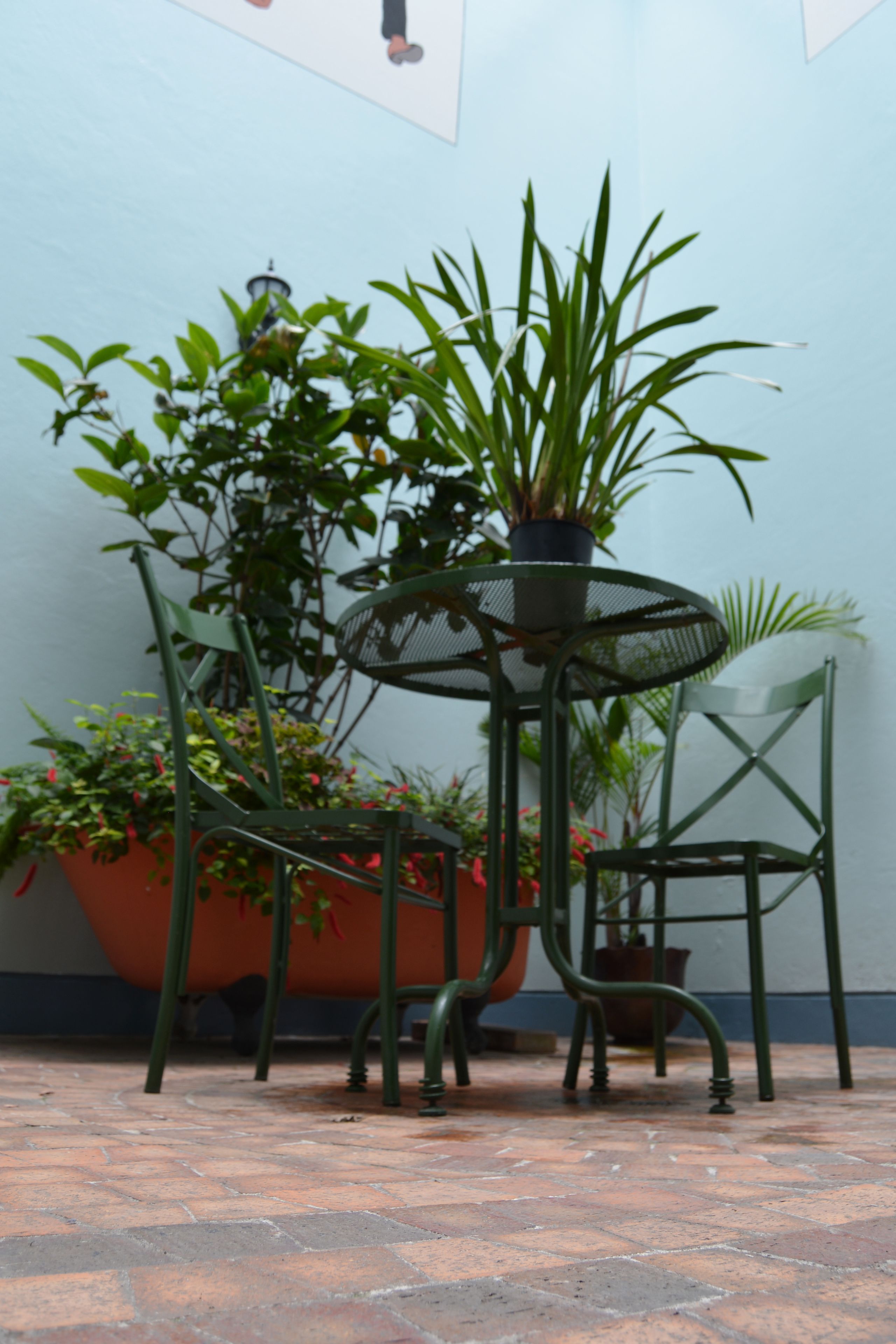 Un pequeño espacio al aire libre con una mesa y sillas de metal, rodeado de plantas en macetas.