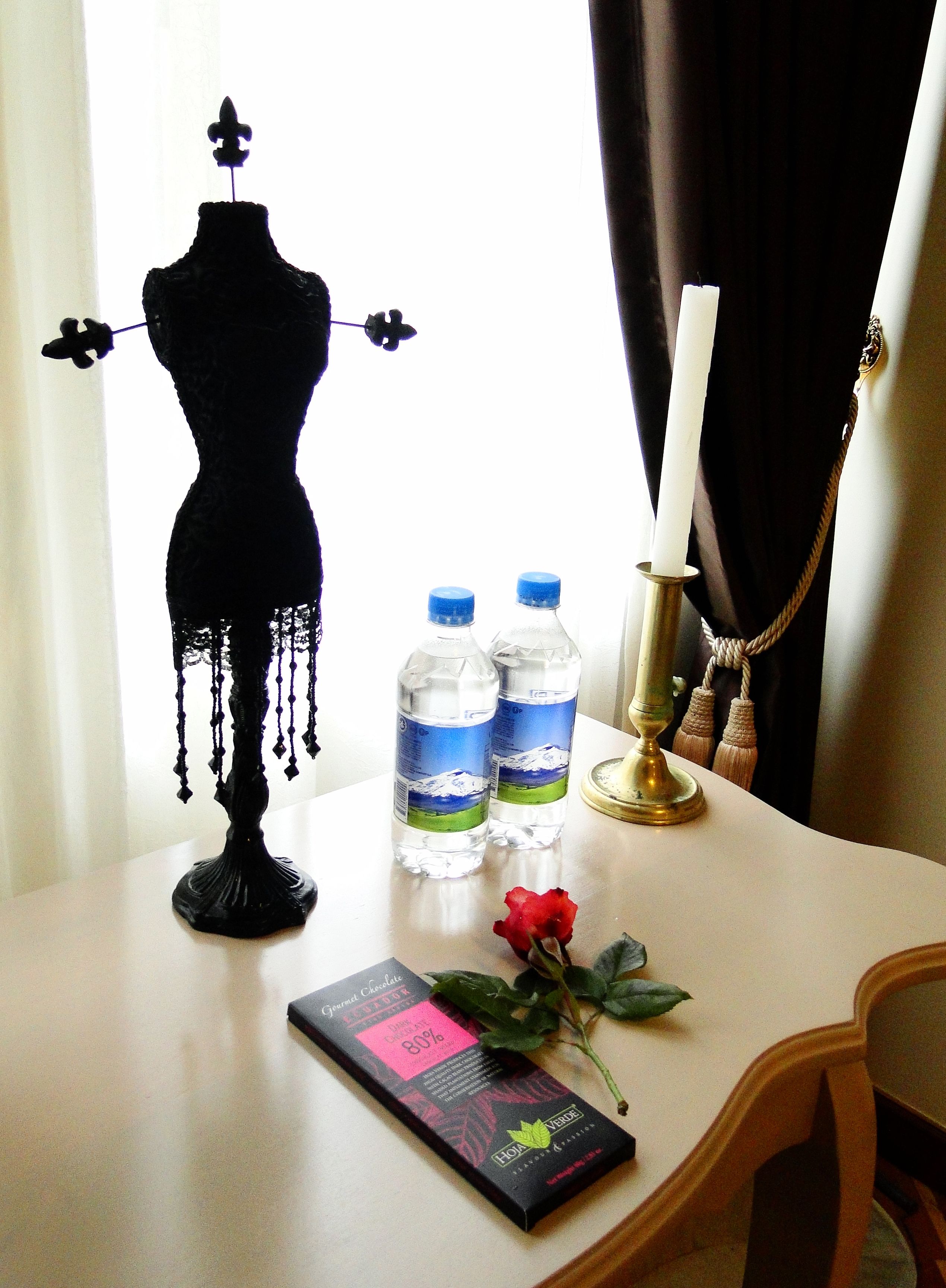 A table with a mannequin, two water bottles, a candle, a rose, and a chocolate bar.