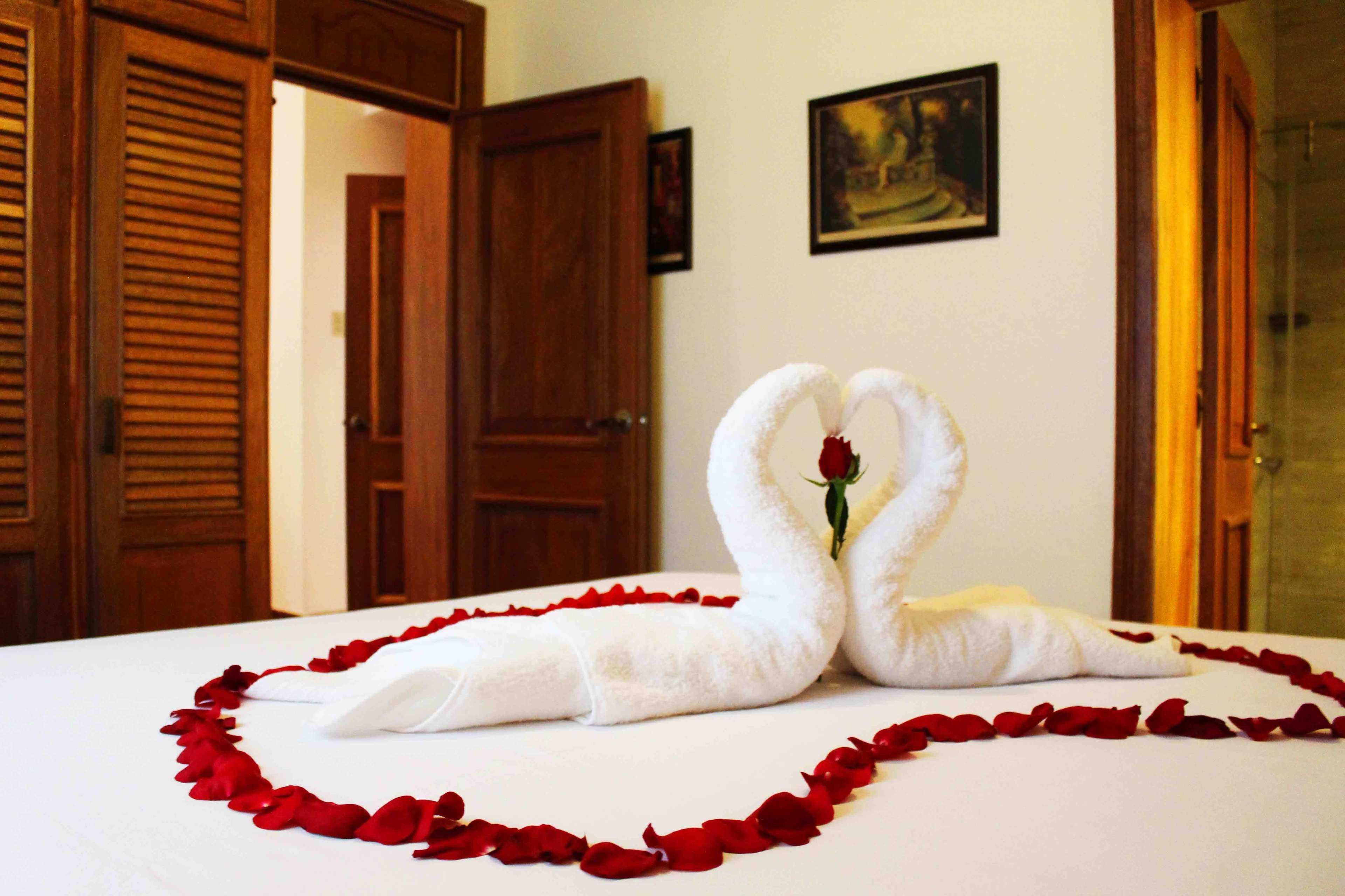 A bed with a heart-shaped arrangement of towels and rose petals.