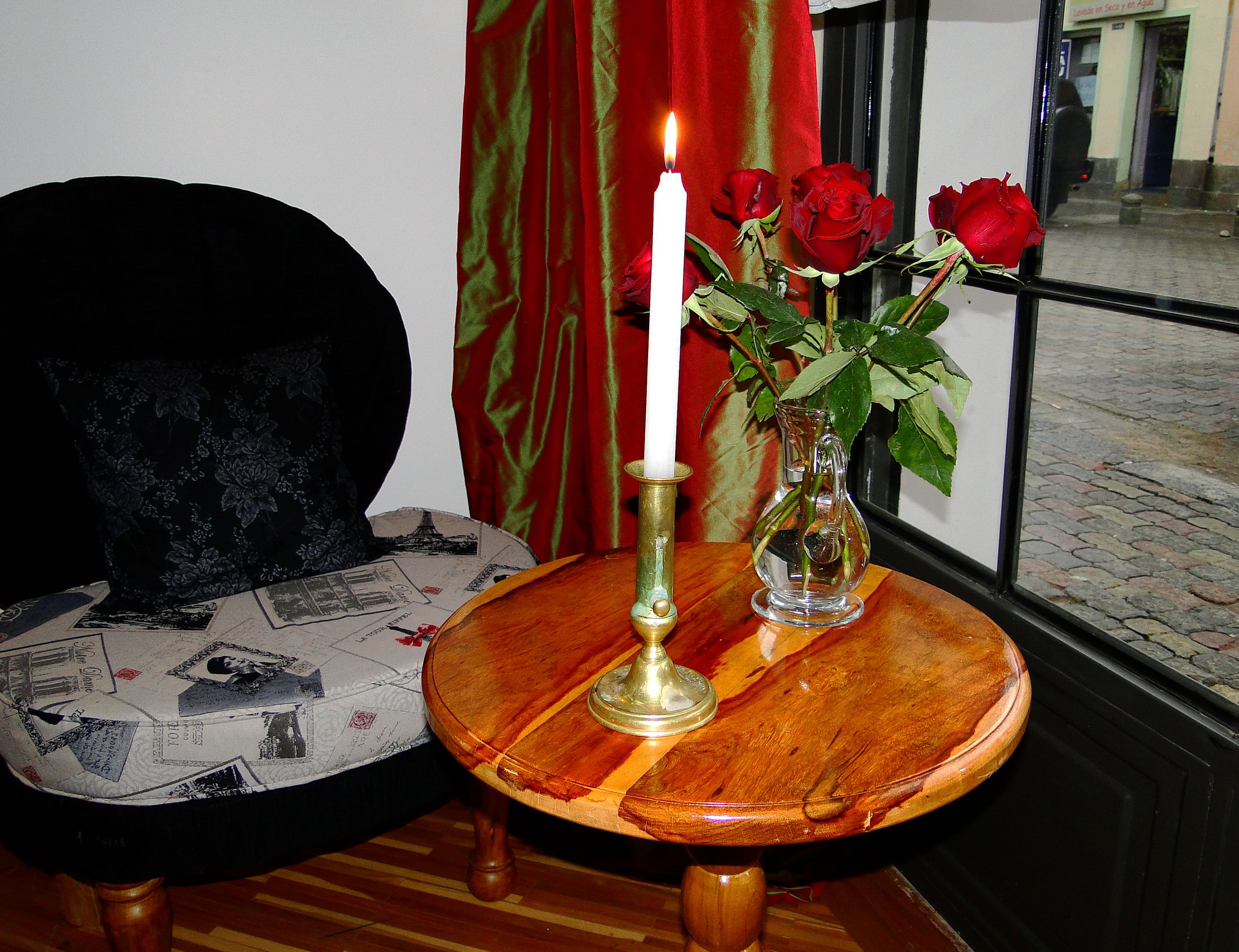 A round wooden table with a white candle and a vase of red roses.