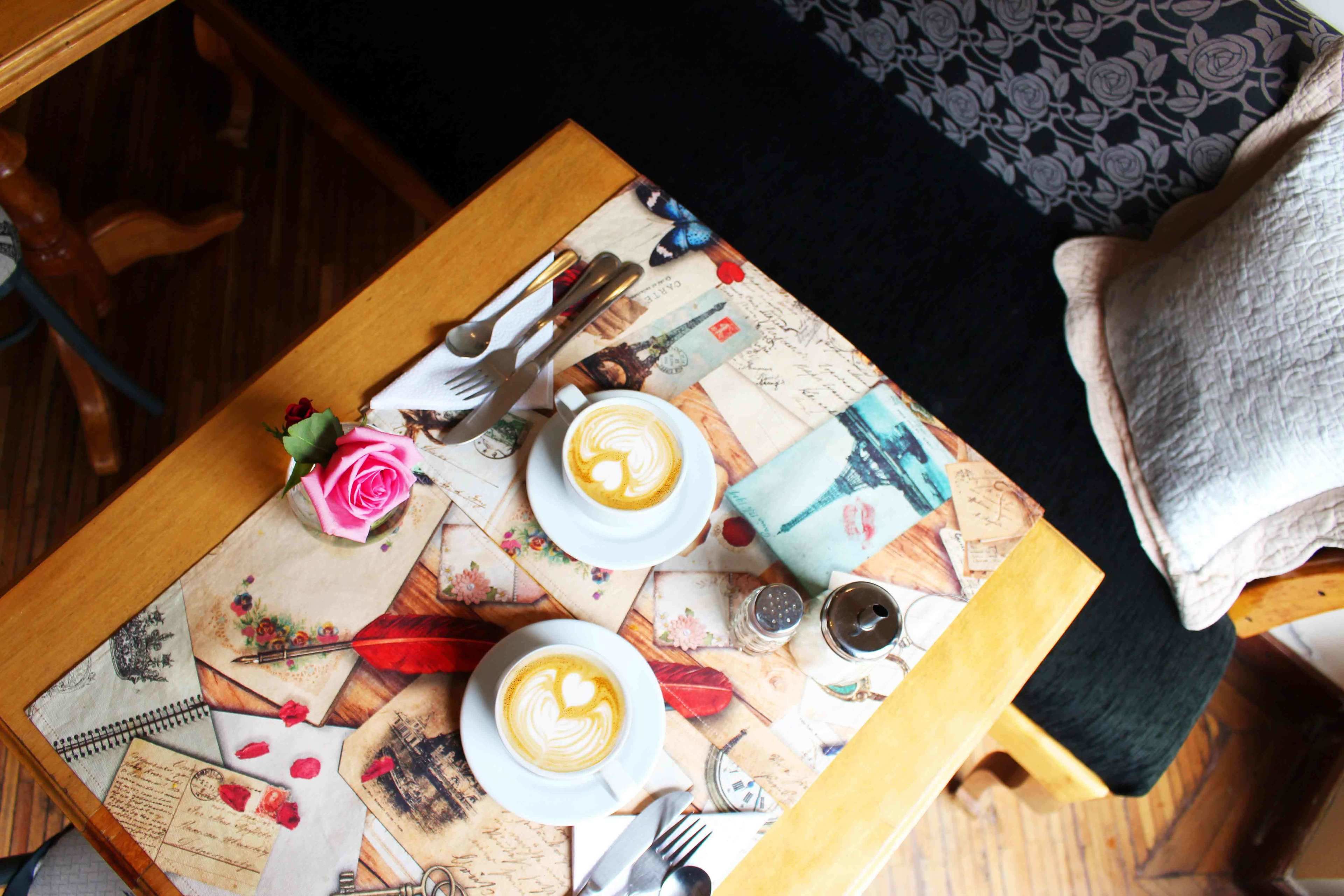A table with two cups of coffee, a rose, and vintage postcards.