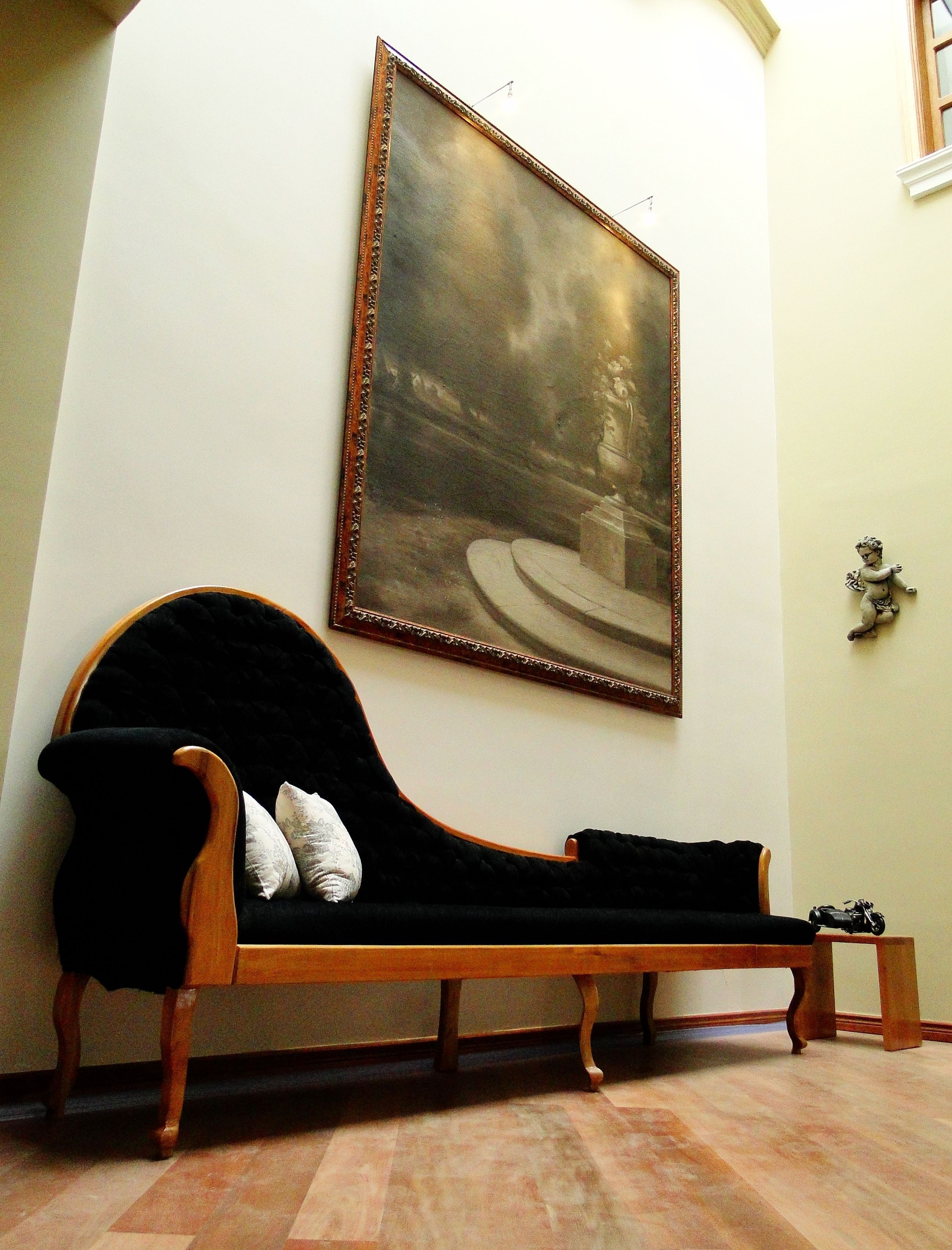 A room with a wooden bench, a large framed painting on the wall, and a small statue on the wall.