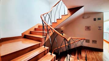 Una escalera de madera con un diseño único de barandilla metálica, que conduce a un rellano con una lámpara.