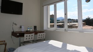 A hotel room with a bed, a desk with two chairs, a TV, and a window with a view of buildings and mountains. - Casa Fusión (La Paz)