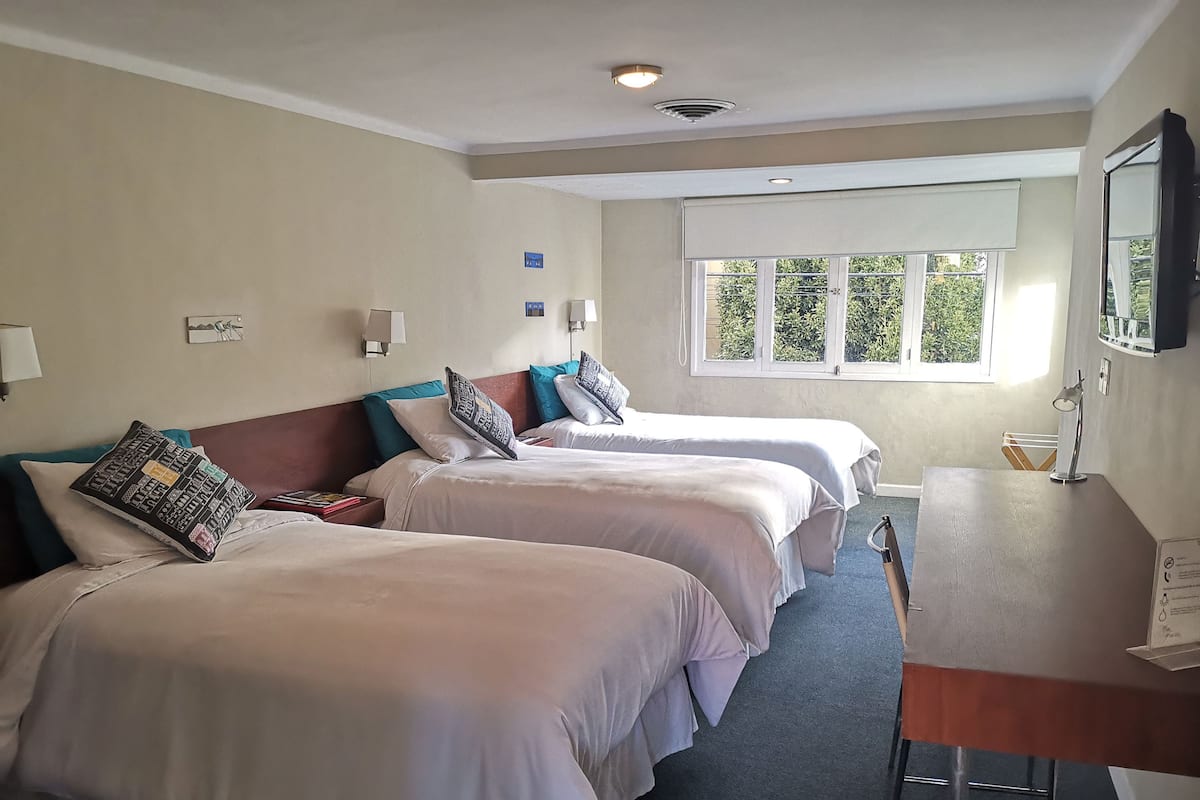 A hotel room with two beds, a desk, and a window with a view of greenery.