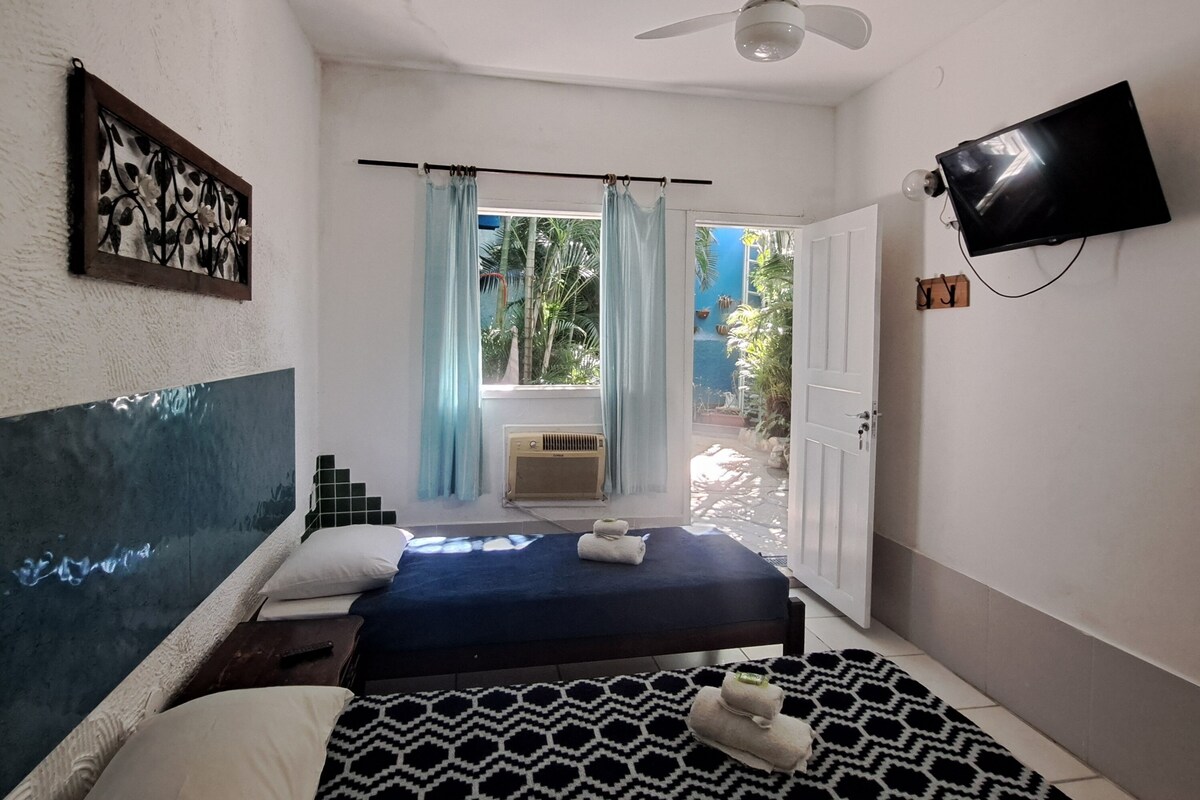 Quarto com cama, ventoinha no teto, televisão e vista para o exterior.