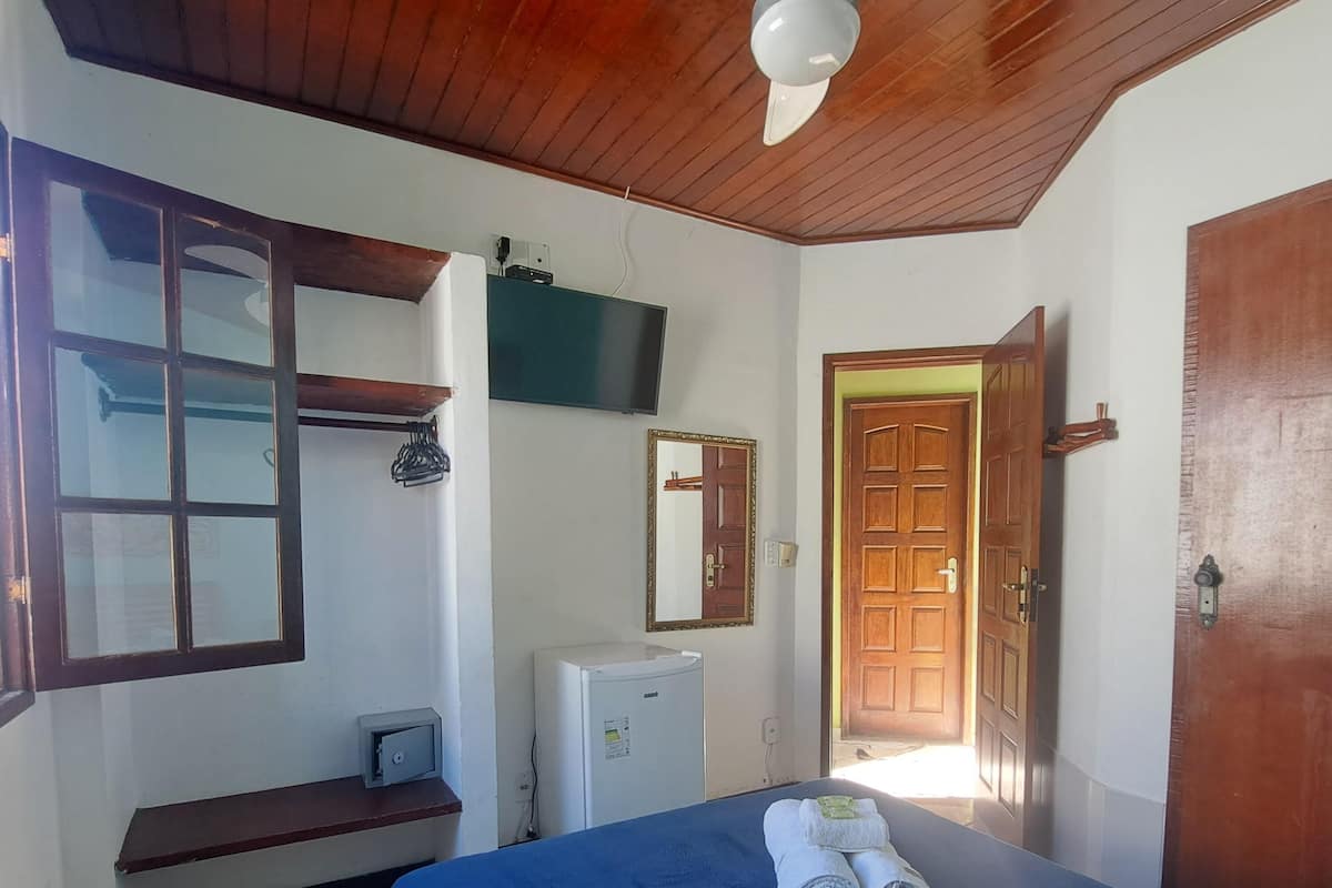 A room with a bed, a ceiling fan, a TV, a refrigerator, a wooden door, and a window.