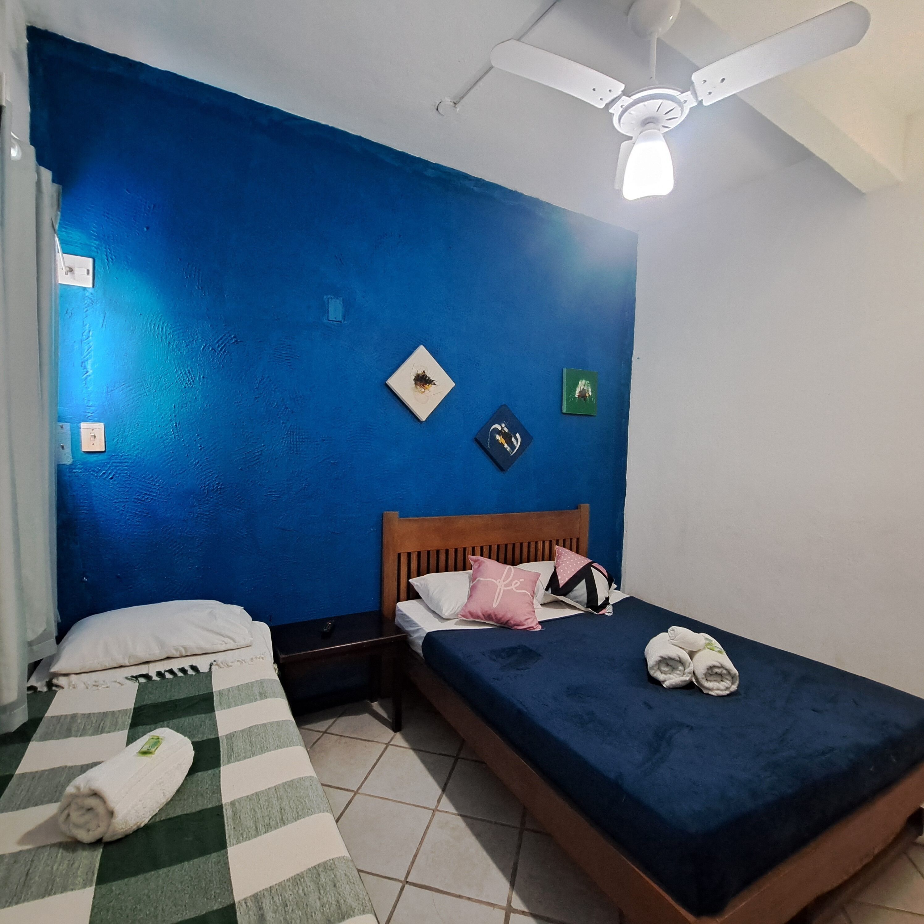 Une chambre avec deux lits, un ventilateur de plafond et un sol carrelé.