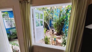 Una stanza con una finestra che si affaccia su un giardino ricco di piante e un muro blu.