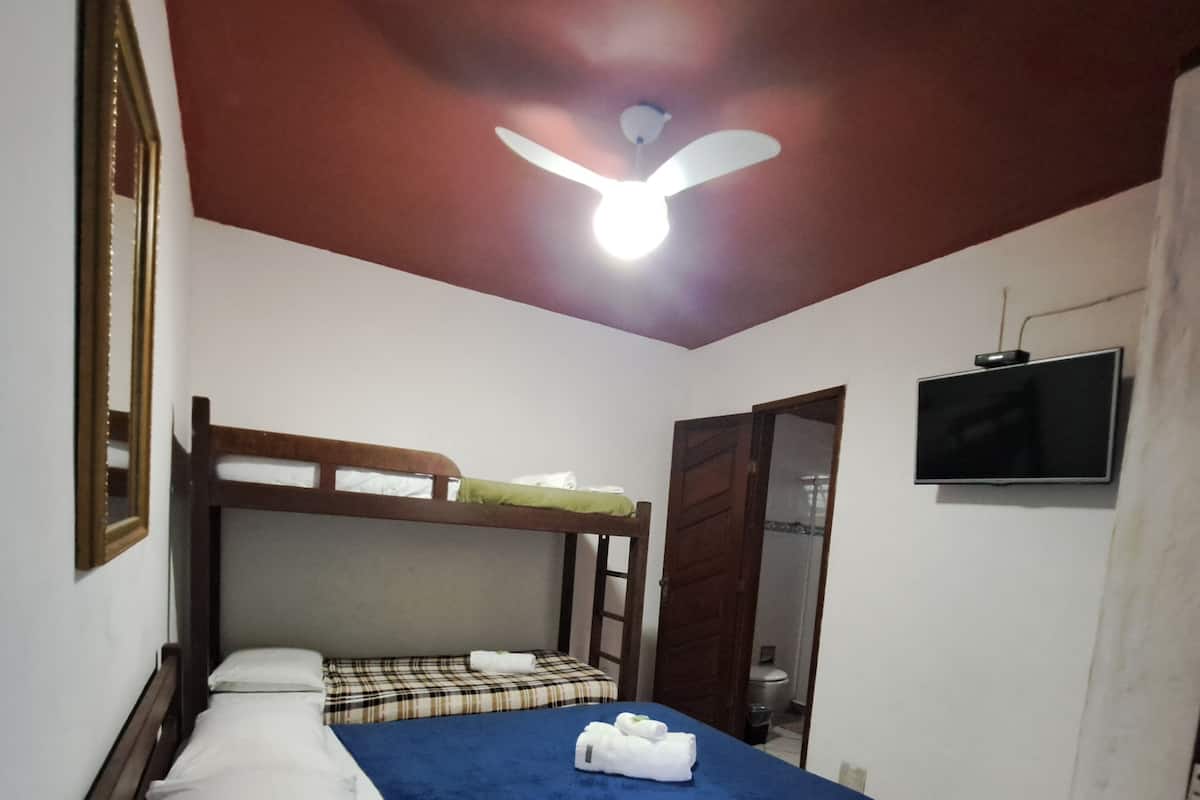 A single bed with a blue bedspread, a wooden headboard, and a ceiling fan.