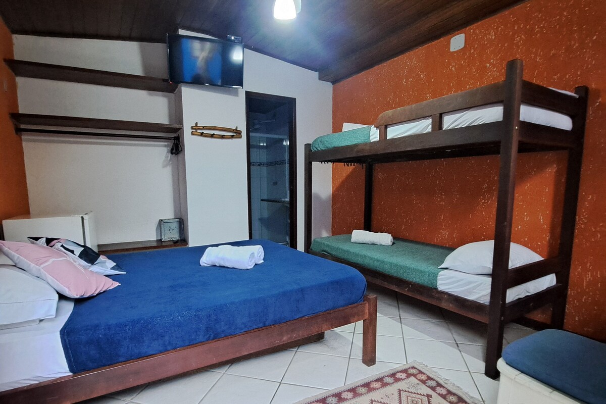 Quarto com beliches, ventilador de teto, televisão e tapete estampado.